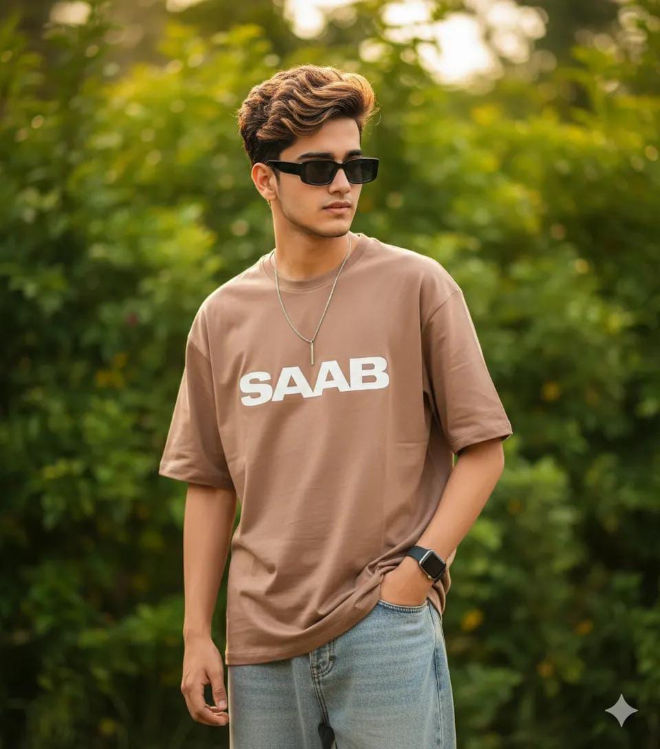 Boys aesthetic photo prompt - stylish young man in a brown oversized SAAB t-shirt, baggy jeans, black rectangular sunglasses and a smartwatch posing outdoors against blurred green trees